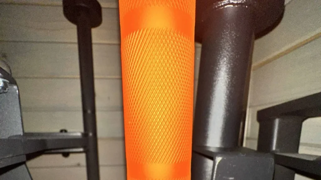 Close-up of the knurling and knurl marks on an orange Cerakote multi-purpose barbell racked in a garage gym