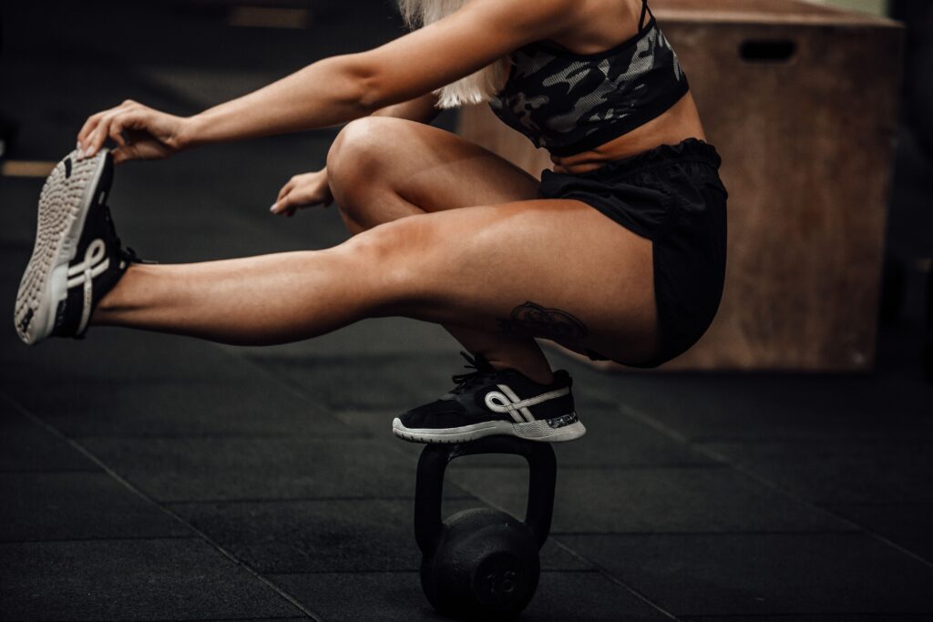 An athletic woman performing balance exercise on kettlebell in a gym.