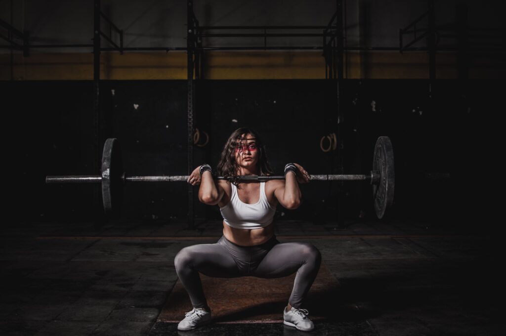A strong female weightlifter squats with a barbell in a dimly lit gym, showcasing power and fitness.