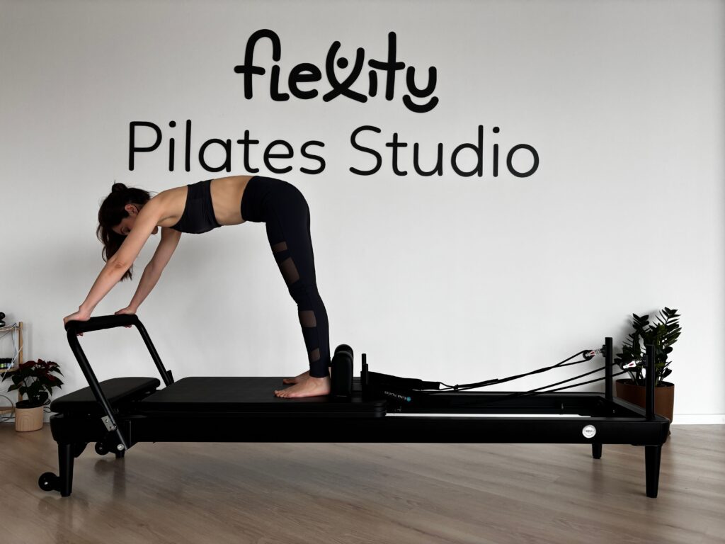 Woman performing Pilates on reformer machine in minimalist studio.