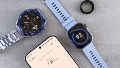 Smartwatch, ring tracker, and smartphone displaying fitness data on a gray surface.