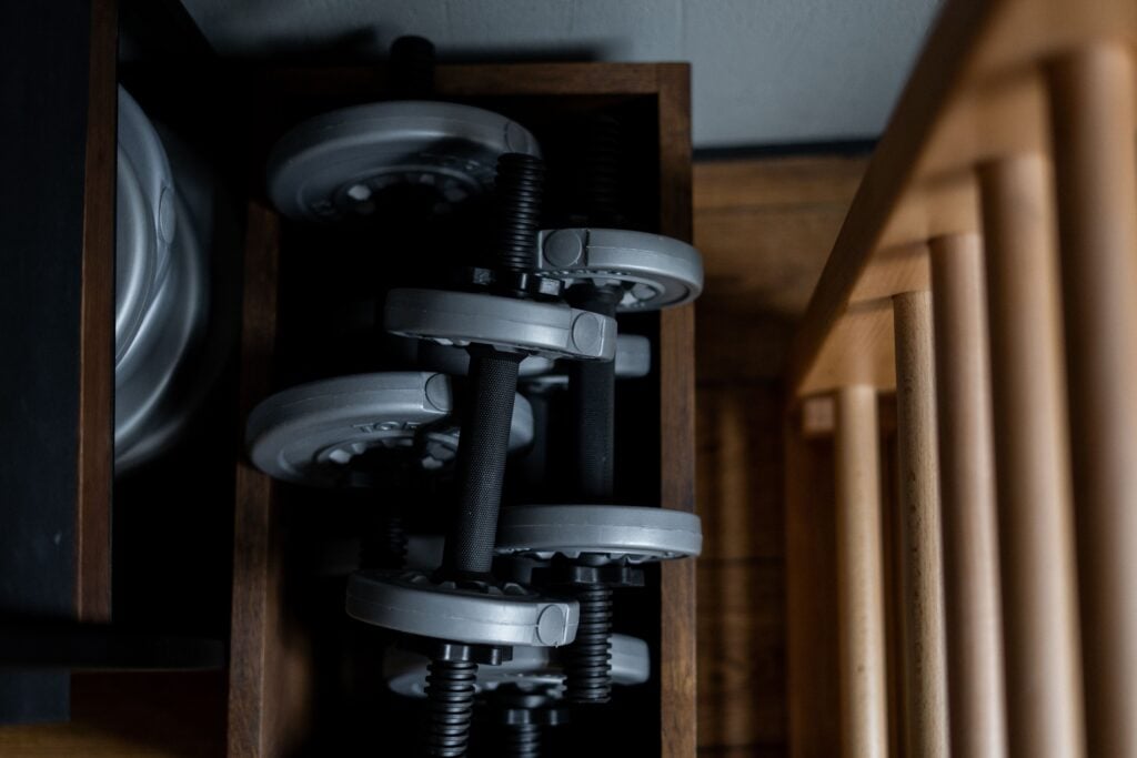 Close-up of stacked dumbbells on a wooden shelf in an indoor gym setting.