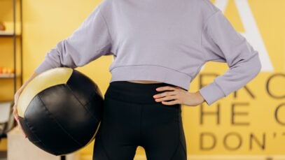 Woman in activewear holding an exercise ball in a gym setting, symbolizing health and fitness.