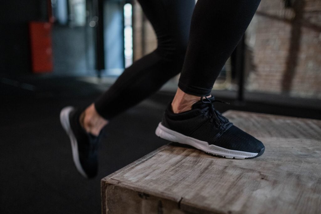 Close-up of an athlete's legs performing a box jump indoors, showcasing athletic footwear and activewear.