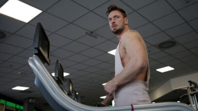 Low angle of muscular adult male athlete in sportswear during training on running machine in modern spacious fitness center while looking away