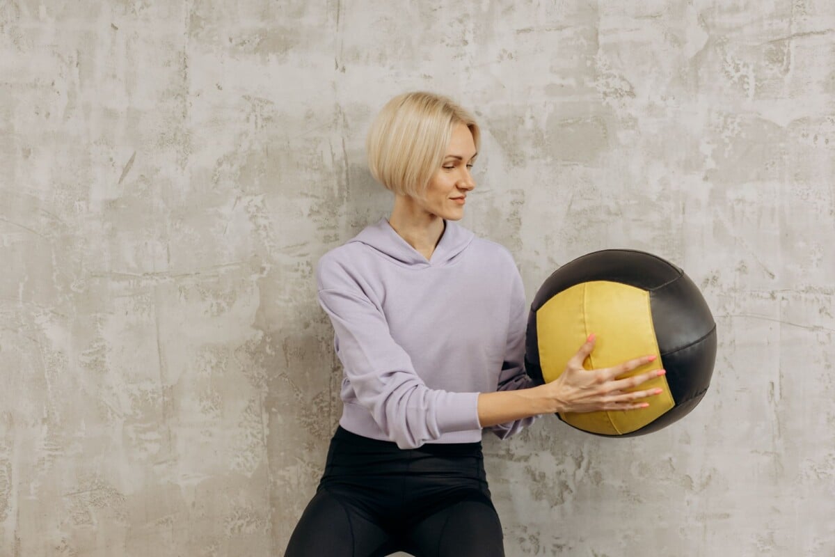 Blonde woman practicing fitness with a medicine ball indoors, emphasizing strength and concentration.