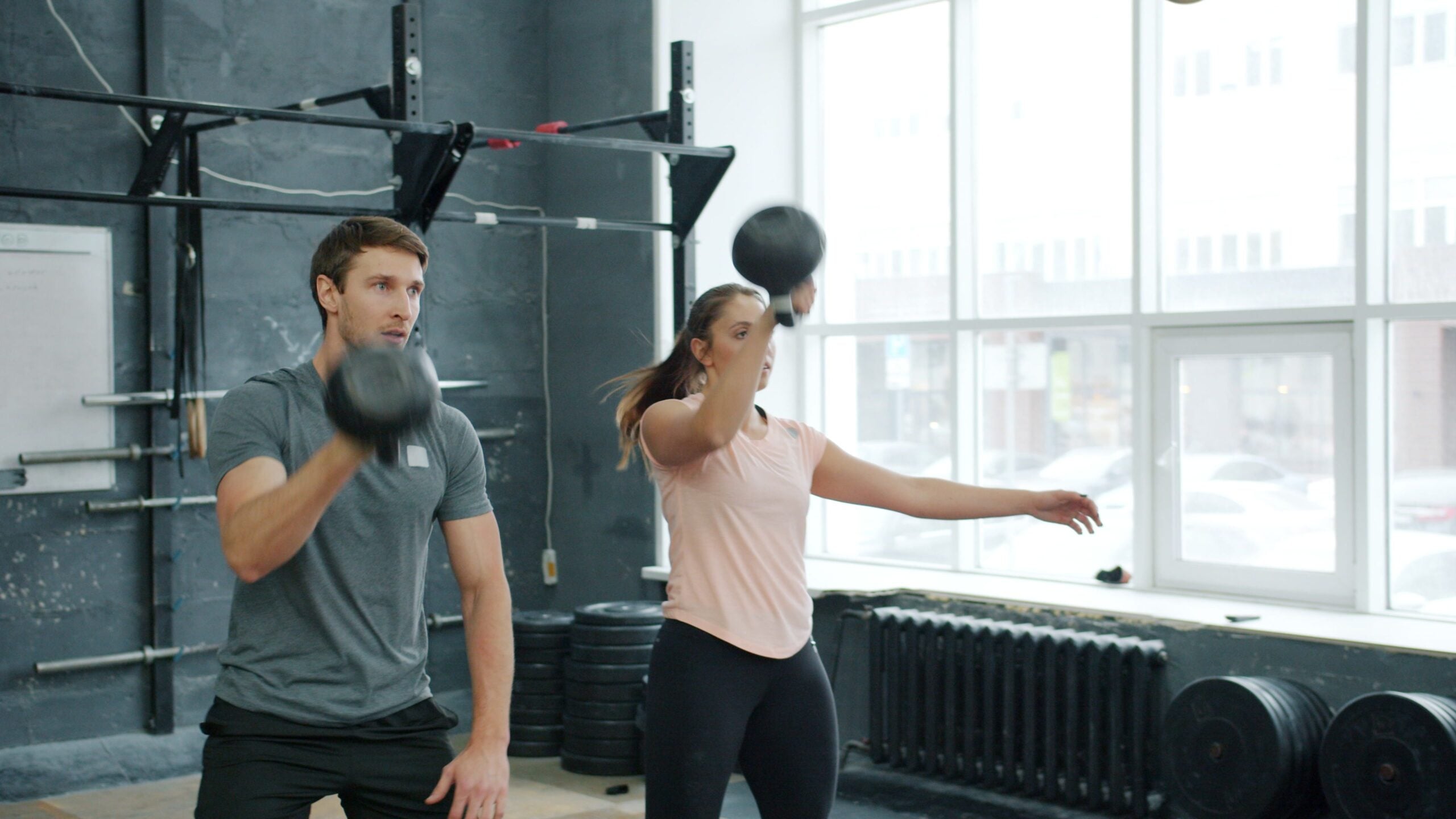 Two adults perform an intense kettlebell workout in a modern gym setting.